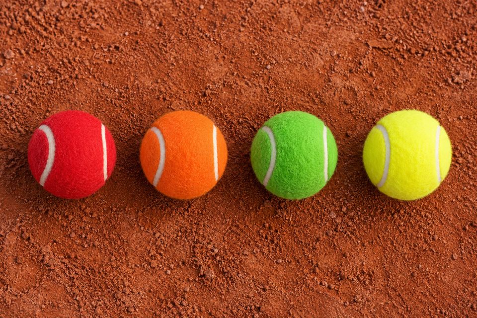 Rode, oranje, groene en gele tennisballen naast elkaar op gravel