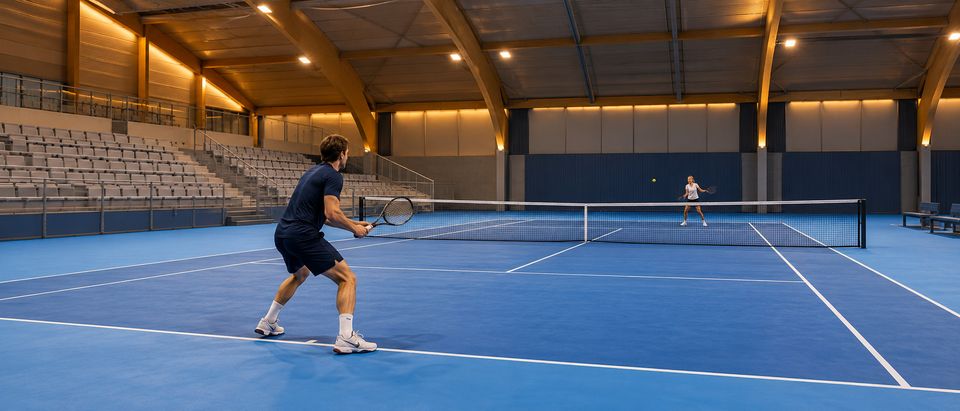 Overdekte tennishal met blauwe hardcourtbanen en warme verlichting Overdekte tennishal met blauwe hardcourtbanen en warme verlichting